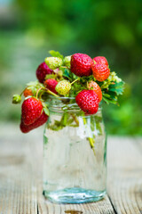 Bouquet of strawberries in small glass jar on the rustic background. Shallow depth of field.