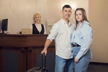 Young couple at check-in desk in hotel. Young woman and man with suitcase stand in front of check-in desk getting ready to check-in.