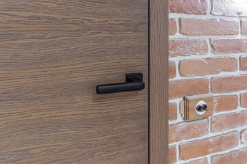 Wood entry door with black handle and industrial brick wall, close up