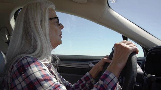 A woman with glasses is driving a car at deserts area during sunshine. Uber driver driving in beautiful place