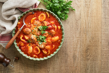 Soup. Fresh tomato soup with meatballs, pasta, vegetables and parsley in green rustic bowl on wooden background. Traditional Italian cuisine. Healthy dinner eating. Top view Autumn cozy dinner concept