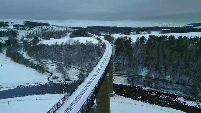 Fly along and under amazing historic structure of Findhorn Viaduct. Railway bridge over river and snowed valley near Tomatin. Scotland, UK