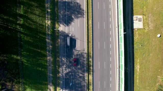 Aerial top down - fast-moving road with speeding cars - an arrow indicating the end of the lane - noise barriers near the street - trees near the roadway.