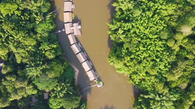 Top down aerial of River kwai floating hotels in brown river surrounded by jungle. Dolly forward, Kanchanaburi, Thailand.