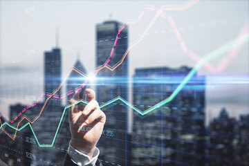 Close up of businessman hand with pen pointing at creative business graph with index and grid on blurry city background. Stock market and financial statistics concept. Double exposure.