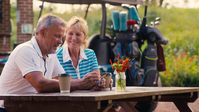 Senior retired couple sitting having coffee after round of golf looking at score card together - shot in slow motion