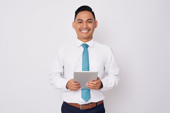Portrait of smiling happy young Asian man in formal wear holding digital tablet and looking at the camera isolated on white background