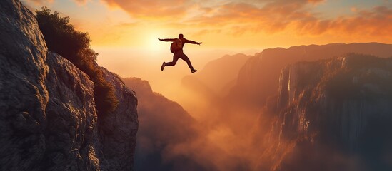 Businessman jumping over a cliff with a sunset in the background. - obrazy, fototapety, plakaty