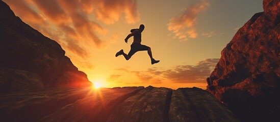 Businessman jumping over a cliff with a sunset in the background.