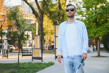 Fototapeta premium Young handsome blinded man walking with stick in town