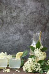 Glass and bottle of lemonade with elder flowers. On light grey background with copy space