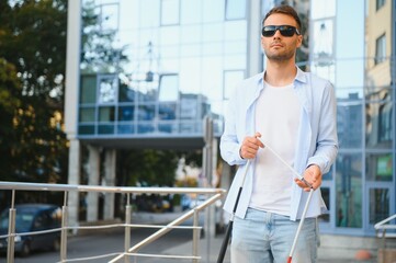 Young handsome blinded man walking with stick in town