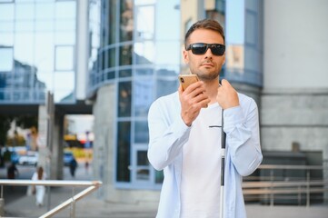 Young blind man with smartphone in city, calling