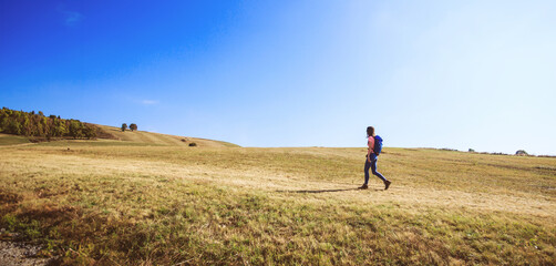 Hiker with backpack walking on rural landscape on sunny autumn day.





