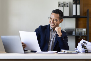 Happy Excited Young business Asian man working at workplace with laptop and papers on desk