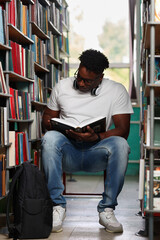 Passionate reader, student, african american studying textbook in university library. Young dark-skinned man reading a book and studying in a public place among shelves