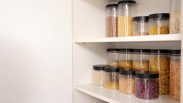 Woman stores containers with different groats on cupboard shelf slow motion. Lady organizes storage in kitchen cabinet before cooking dinner