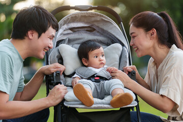 happy parent (father and mother) talking and playing with infant baby in stroller while resting in...
