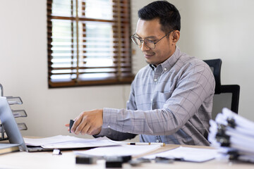 Fototapeta premium Serious and focused financier accountant on paper work inside office, mature business asian man using calculator and laptop for calculating reports and summarizing accounts, 