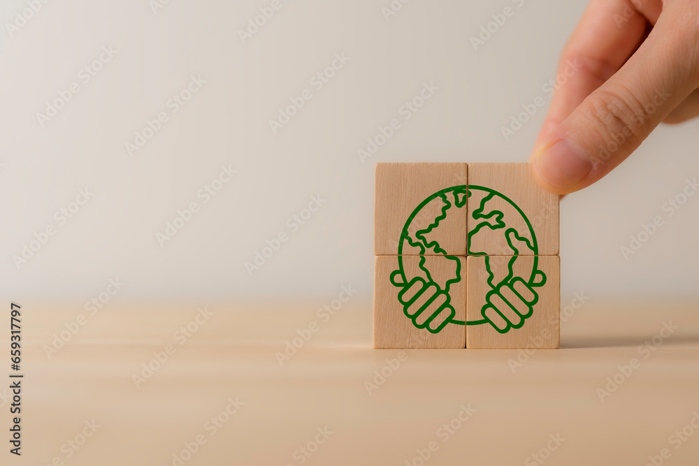 Wall mural Two hands of human holding earth icon on wooden cube blocks. Ecology and world sustainable environment concept. Save of earth, environment protection, world earth day, world environment day.