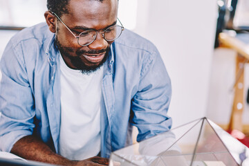 Interested African American freelance man watching plant terrarium in room