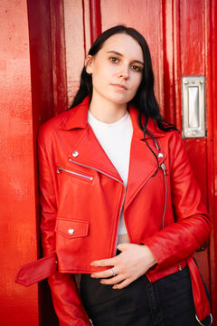Young woman wearing red leather jacket standing in front of door