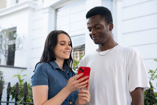 Smiling man with woman using smart phone in front of building