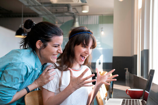 Exycited women looking at laptop in cafe