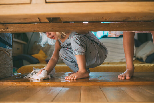 Girl wiping water with rag on hardwood floor at home