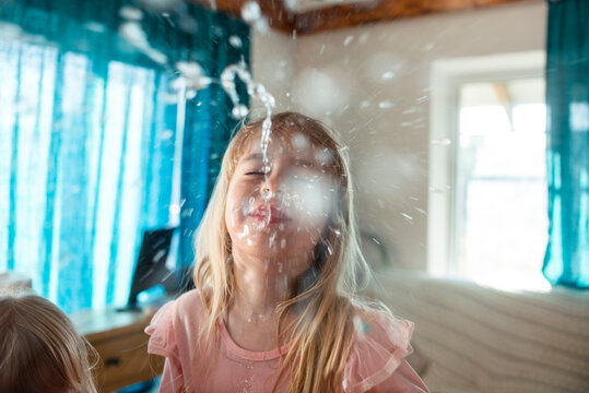 Blond girl laughing and spitting water from mouth at home