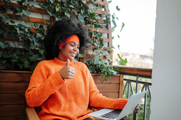 Happy freelancer showing thumbs up gesture on laptop in balcony