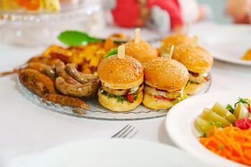 Mini burgers on a plate with french fries and sausages. 