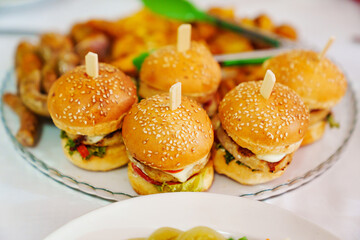 Mini burgers on a plate with french fries and sausages. 