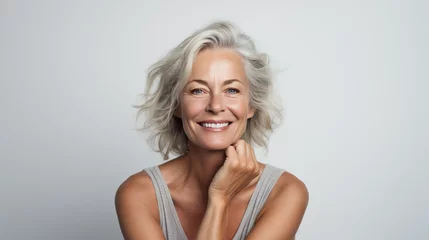 Fotobehang glamour older woman smiling with her hands on her chin, mature model assumed his age with white hair and modern haircut, naturel blue eyes with a happy look, white background  © kiddsgn