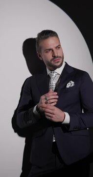 vertical video of attractive businessman touching hands, looking away and over shoulder, touching chin and thinking, holding hand in pocket on grey background