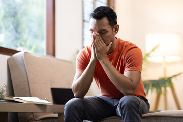 Sad bearded middle-aged man in casual sitting on couch at home, leaning on hands and looking down, upset man having problems, side view, copy space. Loneliness, depression, financial hangover concept