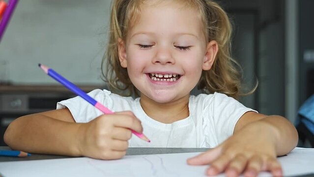 Little girl draws with colored pencils in home. 