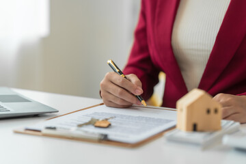 A young Asian real estate agent is reviewing documents and calculating interest rates to inform tenants of monthly installments before entering into contracts to buy or sell real estate.