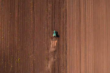 Agricultural tractor vehicle with tiller attached performing field tillage before the sowing season, aerial shot seen from the drone pov