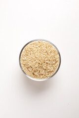 brown rice in glass bowl on white background shot from above