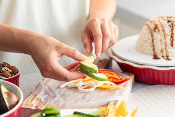 Woman preparing spring rolls in rice paper on kitchen table.