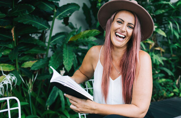 Fototapeta premium Woman laughing reading book at table outdoors