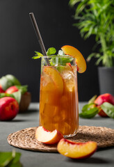 Peach tea with ice and mint on tall glass. Vegan homemade cold summer drink  on a dark background with fresh fruits. Front view.