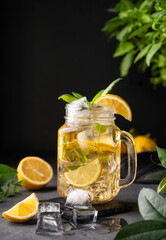 Lemonade drink with fresh lemon, mint and ice in a jar. Refreshing citrus mojito cocktail or cold tea on a dark background. Homemade healthy and detox drink concept.