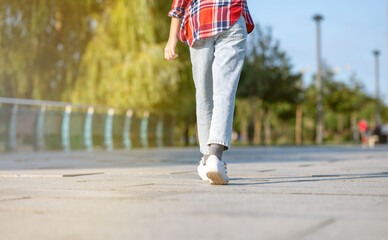 A girl in a plaid shirt jumps and runs along a path in a city park on a sunny summer day. Teenage holiday concept