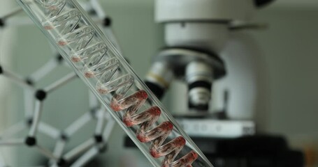 Red chemical liquid flowing through test tube in form of spiral near microscope in laboratory closeup 4k movie. Pharmaceutical technologies concept