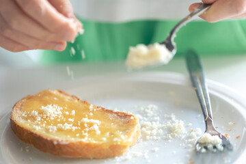 A woman sprinkles a piece of bread with grated cheese.