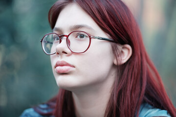 Portrait of a sad girl with glasses. Pensive red-haired teenage girl in a blue T-shirt.
