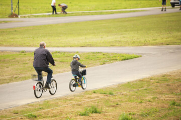 Grandfather and grandson ride bicycles on the asphalt path of the park. Raising the younger generation. Activity of the elderly and children in nature. Sport for a healthy lifestyle. Joyful childhood.