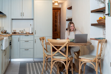 Caucasian female eating delicious breakfast with fresh strawberries while sitting on table and working on her laptop